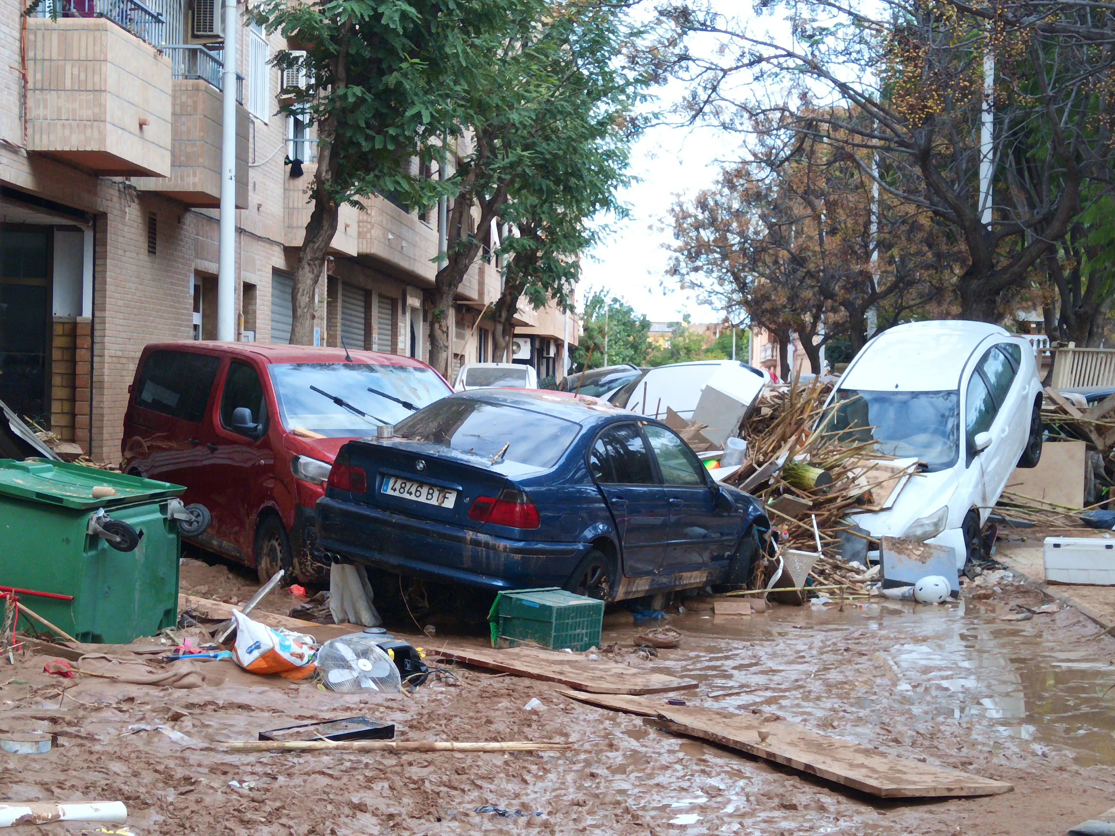 Mud-covered cars pushed against each other and piles of debris in a residential street in Paiporta after the October 2024 flood.